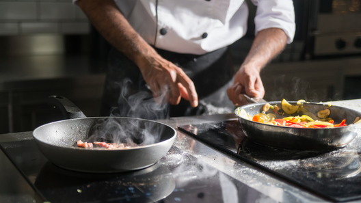 [alt=調理師がフライパンを使用し調理している画像。]
