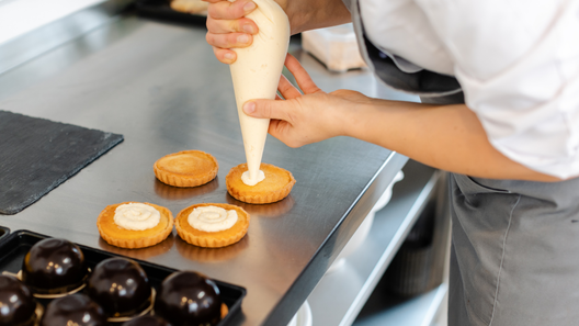 [alt=パティシエがタルトにクリームを絞っている画像。]