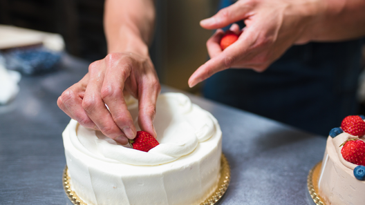 [alt=パティシエがケーキにイチゴを乗せている様子。]

